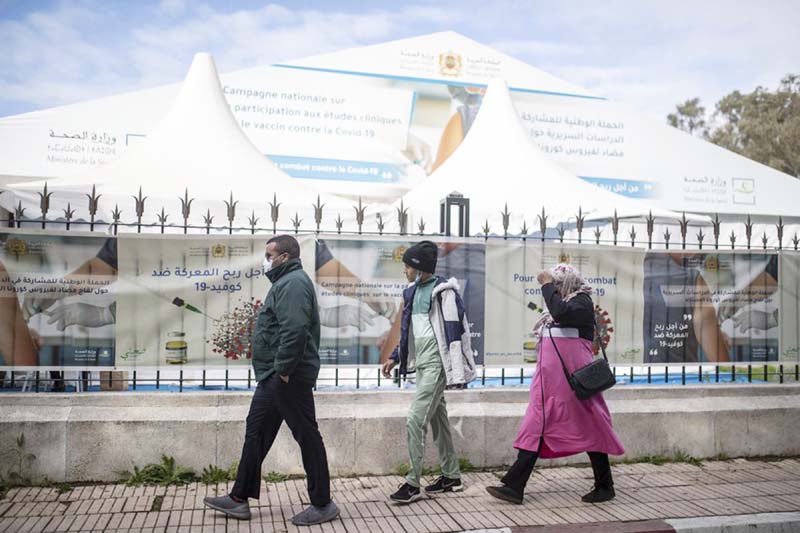 People wearing face masks to prevent the spread of coronavirus walks past a bivouac where clinical trials for covid-19 vaccines are conducted, in Rabat, Morocco.