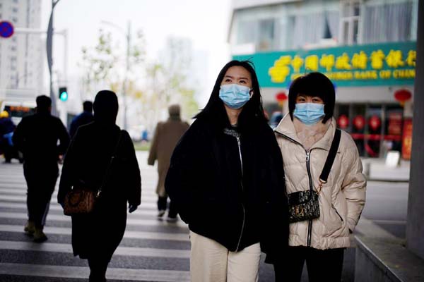 People wearing masks walk across a street, almost a year after the start of the coronavirus outbreak, in Wuhan, Hubei, China.