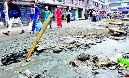 Pedestrians pass beside a road filled with sewage due to sewerage line fault at Banglabazar area of city's Sadarghat on Monday.