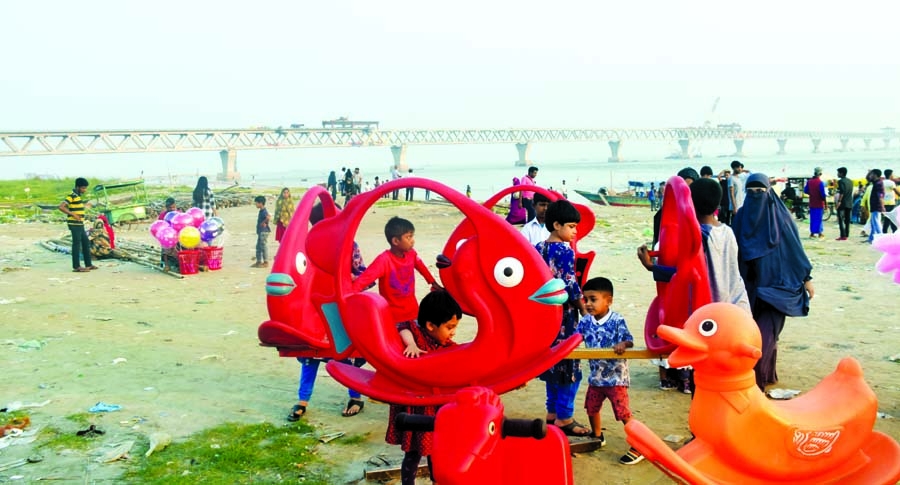 People throng the bank of Padma River at Mawa Ghat in Munshiganj in every weekend, as it has become a new hub of domestic tourism due to the construction of Padma Bridge. This snap taken on Saturday shows children are playing with toys on the river bank