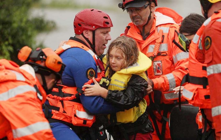 A child is carried to safety by a State Emergency Service member after a Marine Rescue boat rescuing a family from rising floodwaters capsized in strong currents, as the state of New South Wales experiences widespread flooding and severe weather, in the s