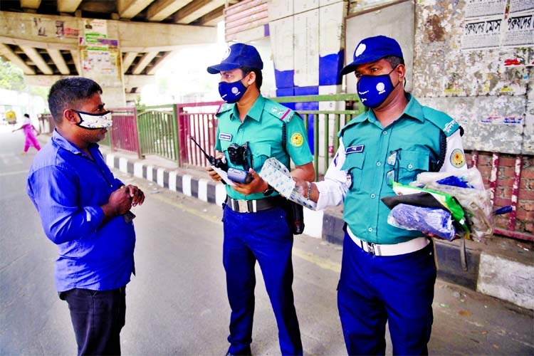 Police stop a pedestrian during lockdown and offer him a surgical mask at Moghbazar area in the capital on Monday.