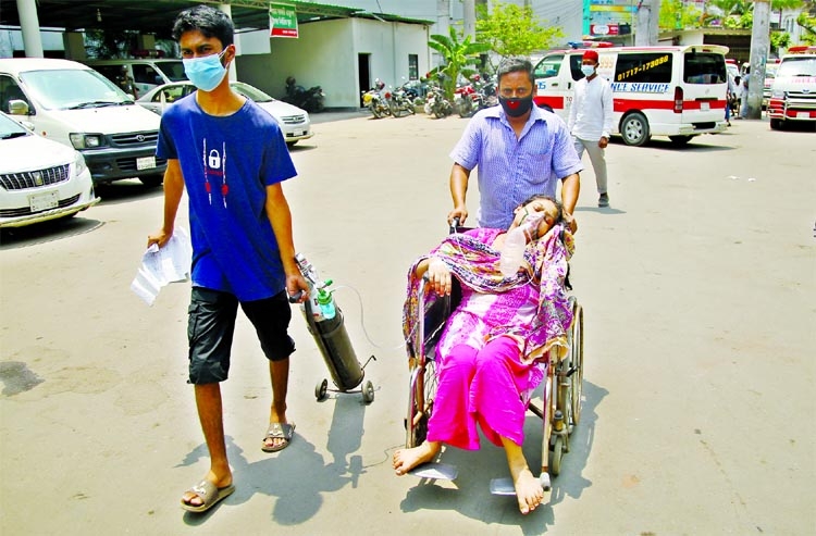 A man takes a patient having respiratory problem in a wheel chair to Dhaka Medical College Hospital with oxygen support on Monday.