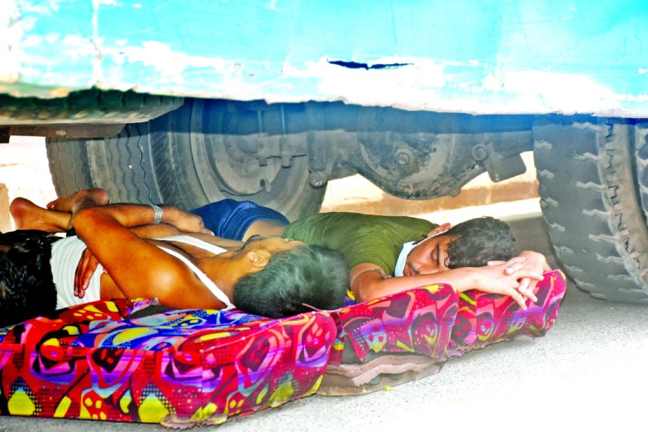 Two transport workers sleeping under a bus taking risk of their lives in order to get relief from heat of summer in front of Bangladesh Bank Colony area in the capital on Tuesday.