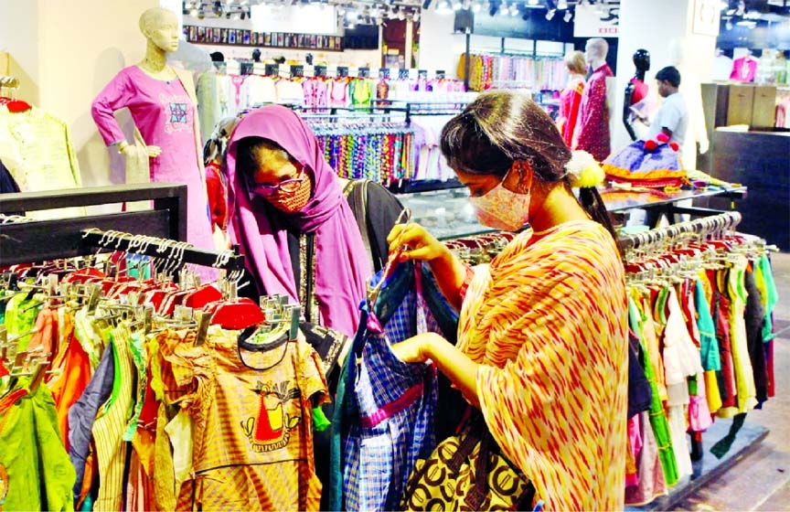 Two women wearing masks browse kids dresses at a fashion outlet at Basundhara City Shopping Complex in the capital on Tuesday.