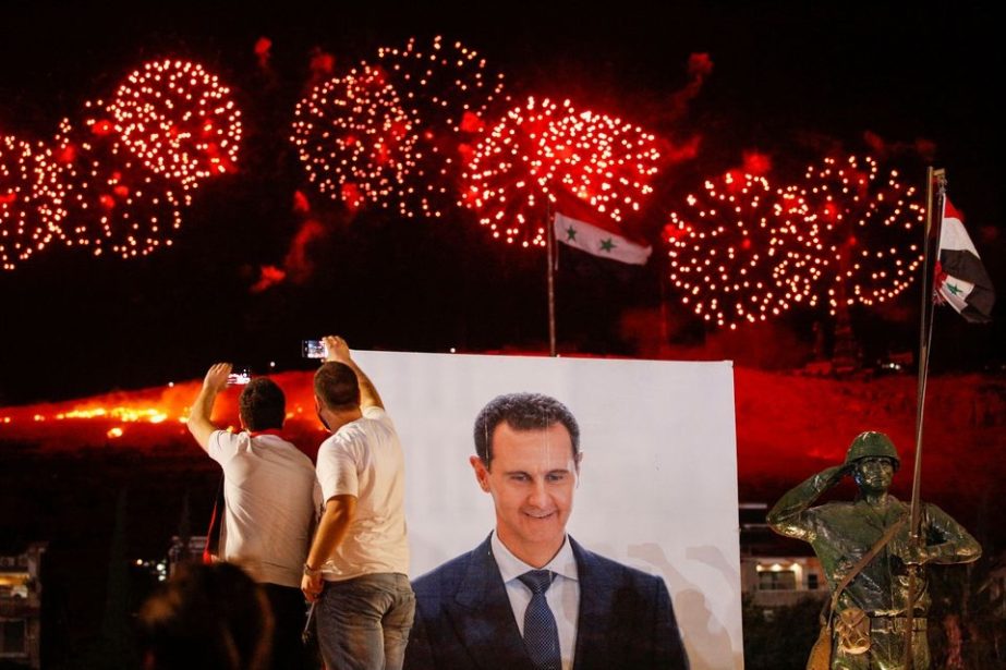 A poster depicting Syria’s president Bashar al- Assad is seen as supporters of of Syria's President Bashar al-Assad celebrate after the results of the presidential election announced that he won a fourth term in office, in Damascus, Syria, May 27, 2021