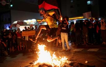 A man jumps over a burning doll depicting Brazilian President Jair Bolsonaro during a protest against him, in front of the Museum of Modern Art in Sao Paulo, Brazil.