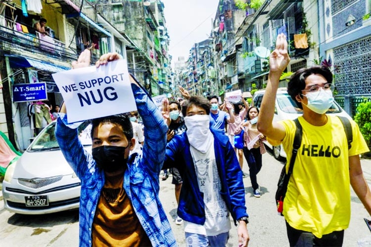 A protester holds a sign in support of the National Unity Government as others make the three-finger salute during a demonstration against the military coup in Yangon, Myanmar.