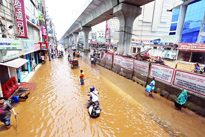 People wade through a waterlogged street at Begum Rokeya Sarani, Mirpur, in the capital Dhaka. Heavy monsoon rain lashed the capital on Saturday morning, inundating low-lying areas and disrupting road traffic.