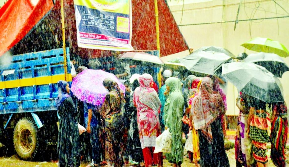 Defying heavy downpour, people of limited income group standing in a long queue to buy essentials from the truck of Trading Corporation of Bangladesh (TCB) in front of Jatiya Press Club in the city on Wednesday.