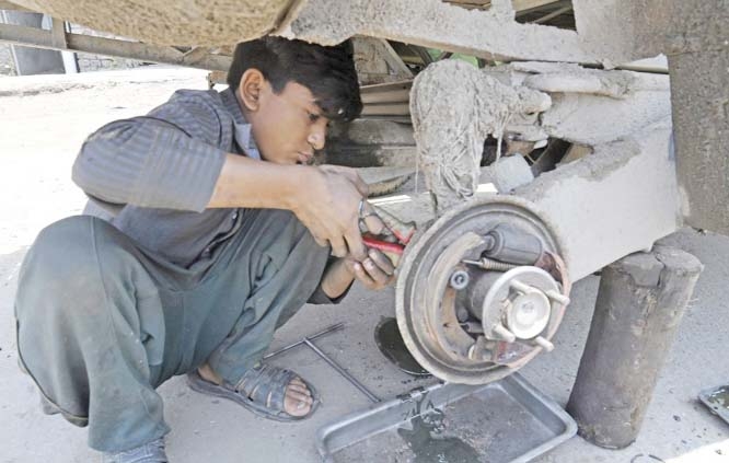 A boy works on a vehicle at a roadside in Lahore on Thursday.