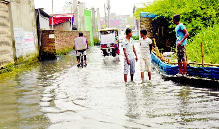 People wade through rain water at Matuail area under DND embankment in the capital on Wednesday.