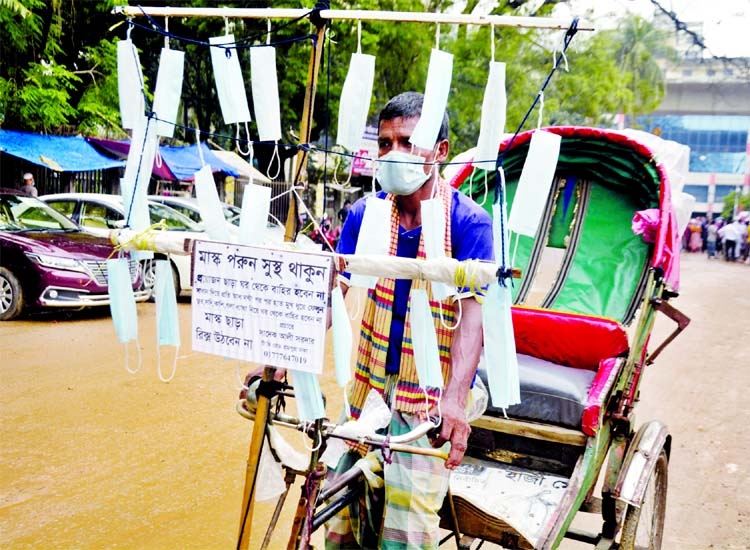 A conscious rickshaw puller sells masks hanging a leminated placard that showed 'Wear Mask, Stay Safe' in front of the Secretariat in the capital on Wednesday.