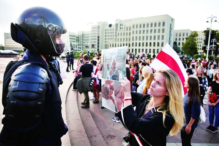 A woman holds a poster with pictures of injured persons in front of a law enforcement officer during a rally against police brutality following protests to reject the presidential election results in Minsk, Belarus.