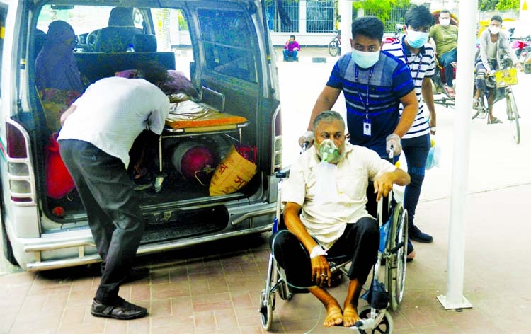 A man carries a patient in a wheel chair who came from outside Dhaka by an ambulance having respiratory problem with oxygen support. This photo was taken from in front of DNCC Dedicated Covid Hospital at Mohakhali.