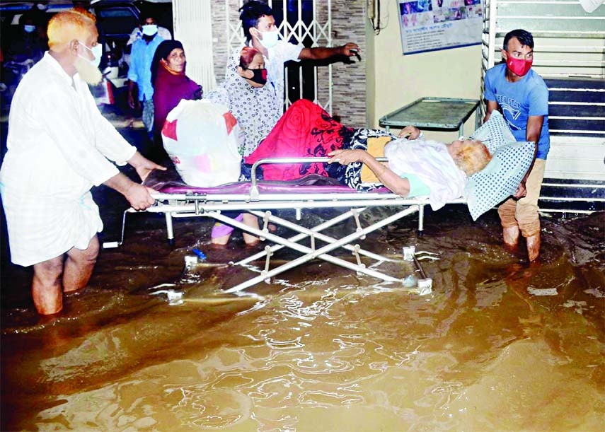 Two people take a Covid patient lying on a stretcher in a waterlogged space in front of Ma O Shishu Hospital at Agrabad area in Chattogram on Saturday after a short spell of rain.