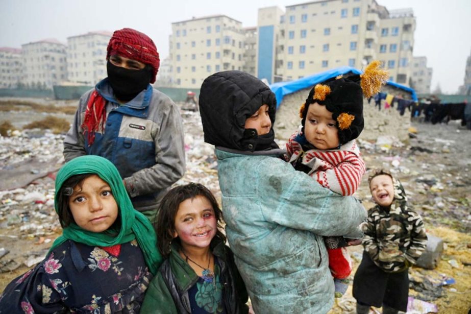 Afghan children IDPs stand outside their temporary mud house at a refugee camp in Kabul