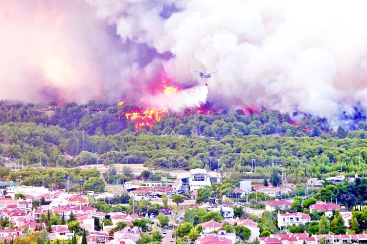 A firefighting helicopter douses a wildfire in the area of Varympompi, Athens, Greece.