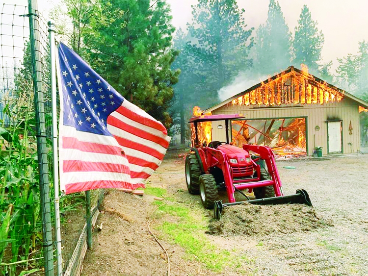 A red tractor is left behind as a home burns outside of Taylorsville in Plumas County, California, US that was impacted by the Dixie Fire on Friday.