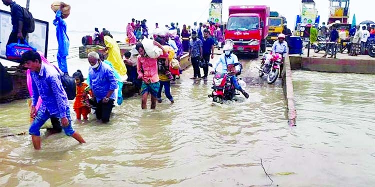 People along with motor vehicles wade through water logged ferry ghat as low-lying areas of Borguna district has been inundated by new moon tide.