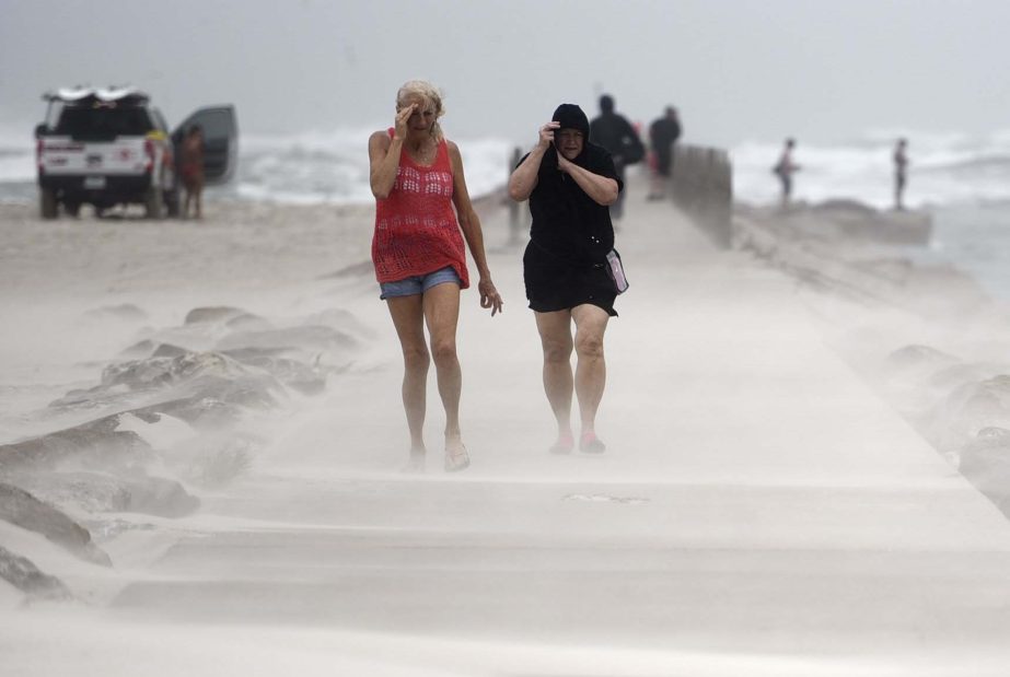 People shield their faces from wind and sand ahead of Hurricane Nicholas, Monday, on the North Packery Channel Jetty in Corpus Christi, Texas. AP photo