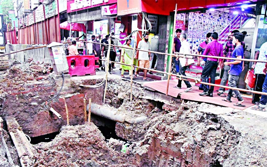 People walk past a dilapidated road in front of Topkhana Surgical Market in the capital on Sunday.