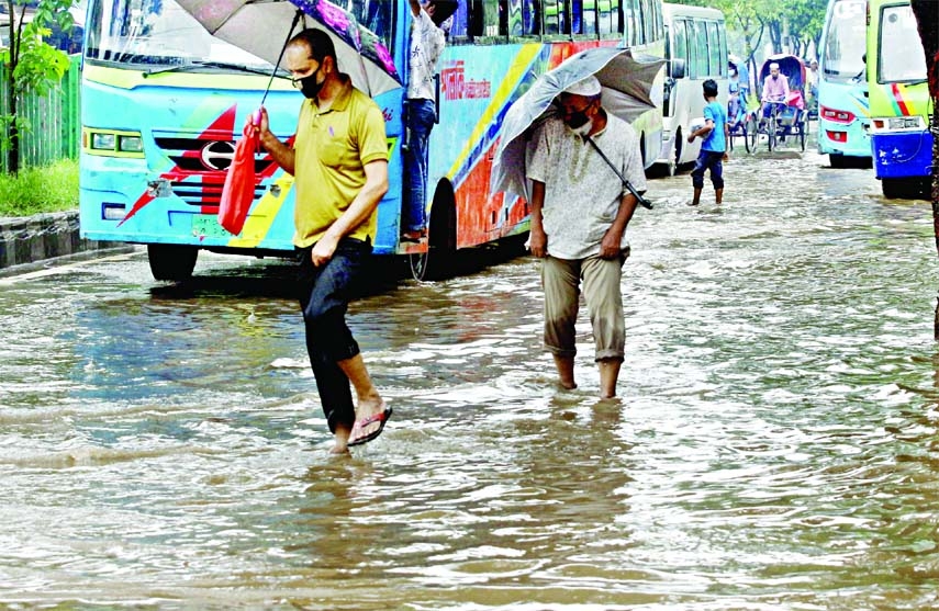 Pedestrians walk through a waterlogged road after a brief spell of rain at Arambagh area in the capital on Monday.