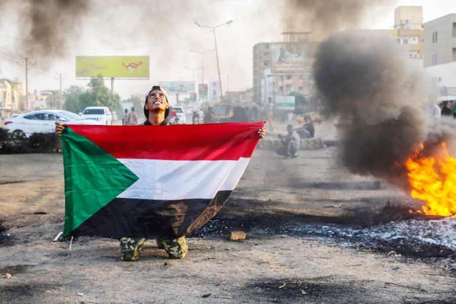 A Sudanese protester holds the national flag next to burning tyres during a demonstration in the capital, Khartoum, Sudan recently. Agency photo