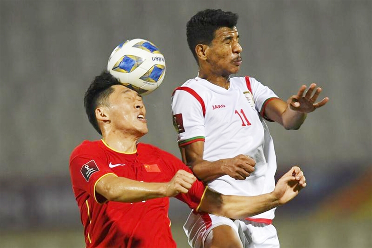 China's Zhu Chenjie (left) and Oman's Issam Al Sabhi jump for the ball during a qualifying soccer match for the FIFA World Cup Qatar 2022 between China and Oman in Sharjah, the United Arab Emirates on Thursday.