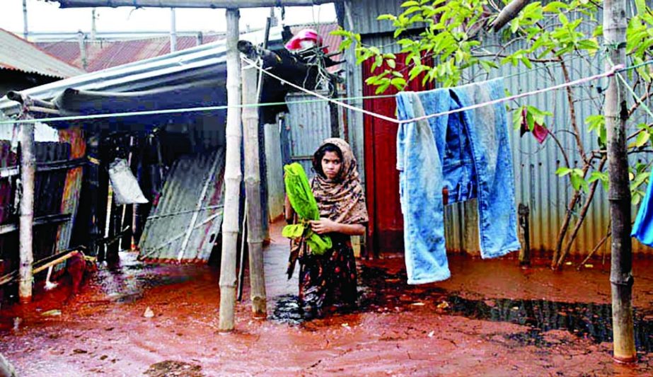 A girl stands in a knee-deep waterlogged house at Jurain Dhaka Match Factory workers colony area on Tuesday as there is no drainage system. NN photo