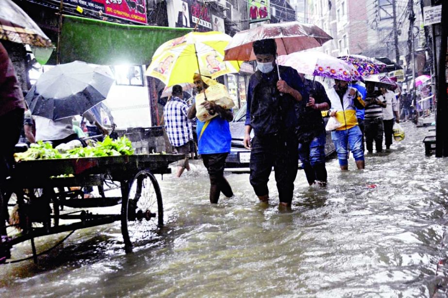 People walk through knee-deep water on a road in the capital's Siddique Bazar amid incessant rains caused by Cyclone Jawad on Monday. NN photo