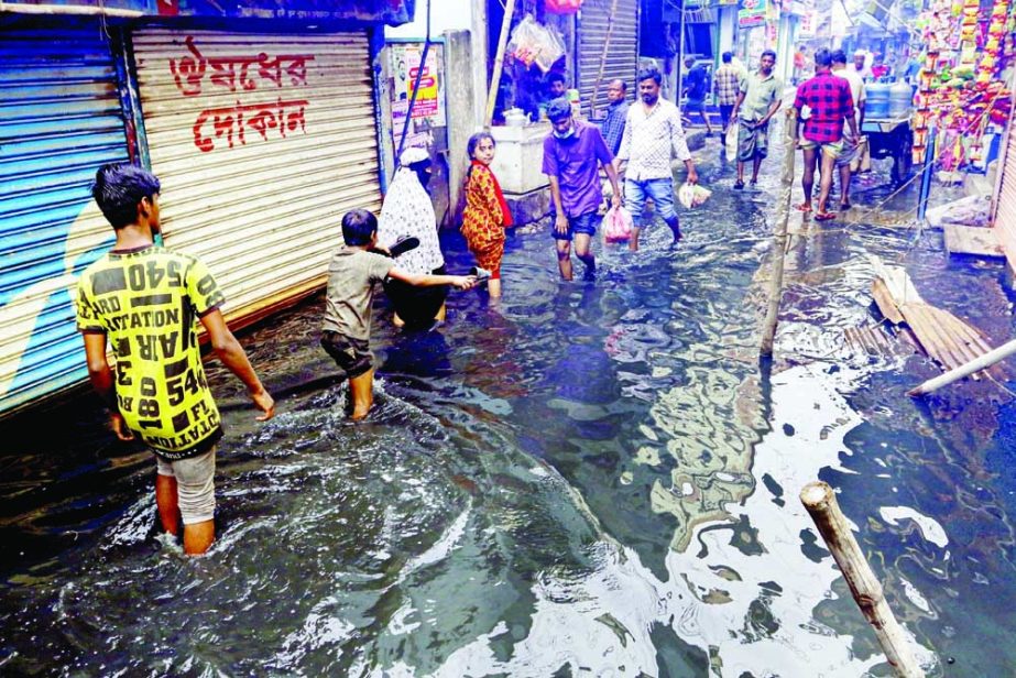 Pedestrians struggle to move through knee-deep water on a road submerged by the recent rainwater at Nama Shyampur area in the capital on Saturday. NN photo