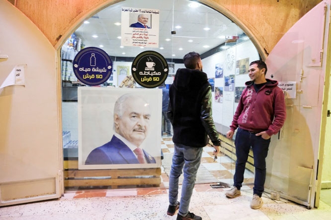 Two men stand beside a picture of Libya's eastern commander and presidential candidate Khalifa Haftar, pasted on the glass facade of a cafe in Benghazi.