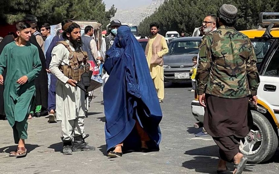 Taliban forces block the roads around the airport, while a woman with Burqa walks passes by, in Kabul, Afghanistan. File photo