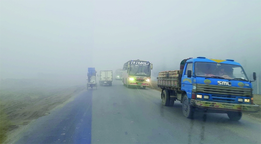 Vehicles plying with the headlights on even in day hours through dense fog at Golchottor area of Hatikumrul on Dhaka-Bogura Highway on Monday.