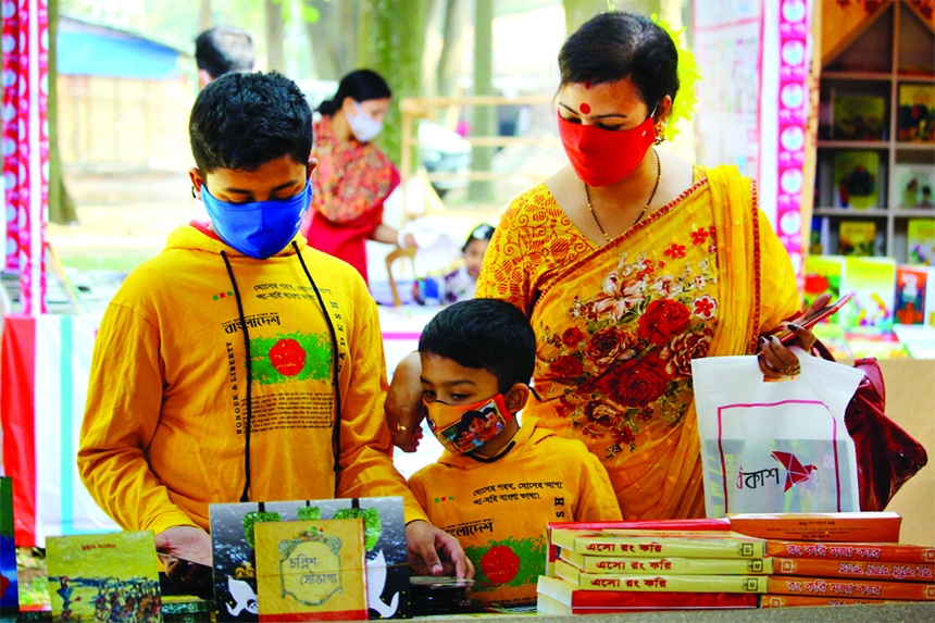 Two children, accompanied by her mother, browse a book at a stall at the Ekushey Book Fair on Friday.