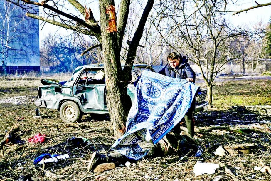 A man uses a carpet to cover a body stretched out on the ground after bombings on the eastern Ukraine town of Chuguiv. Agency photo