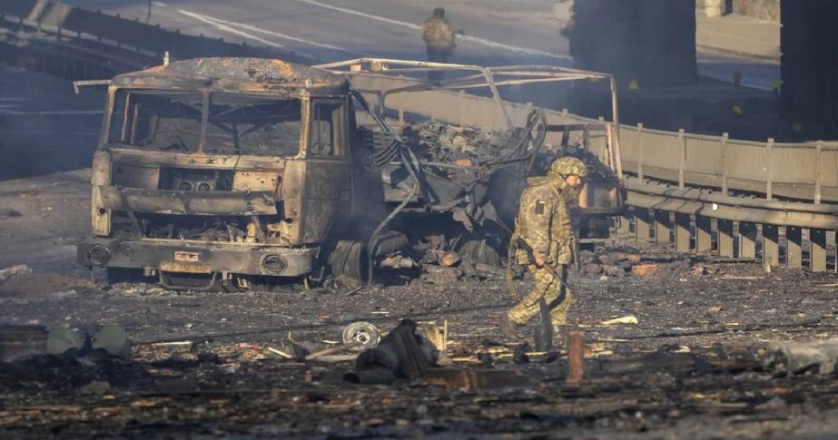 A Ukrainian soldier walks past debris of a burning military truck, on a street in Kyiv, Ukraine, Saturday, Feb. 26, 2022.