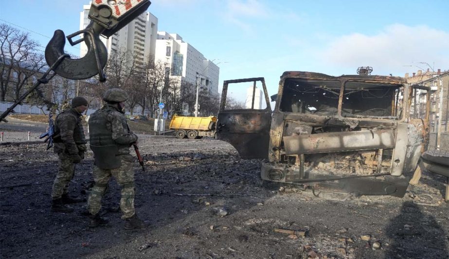 Ukrainian soldiers stand next to a burnt military truck, in a street in Kyiv, Ukraine, Saturday, Feb. 26, 2022.