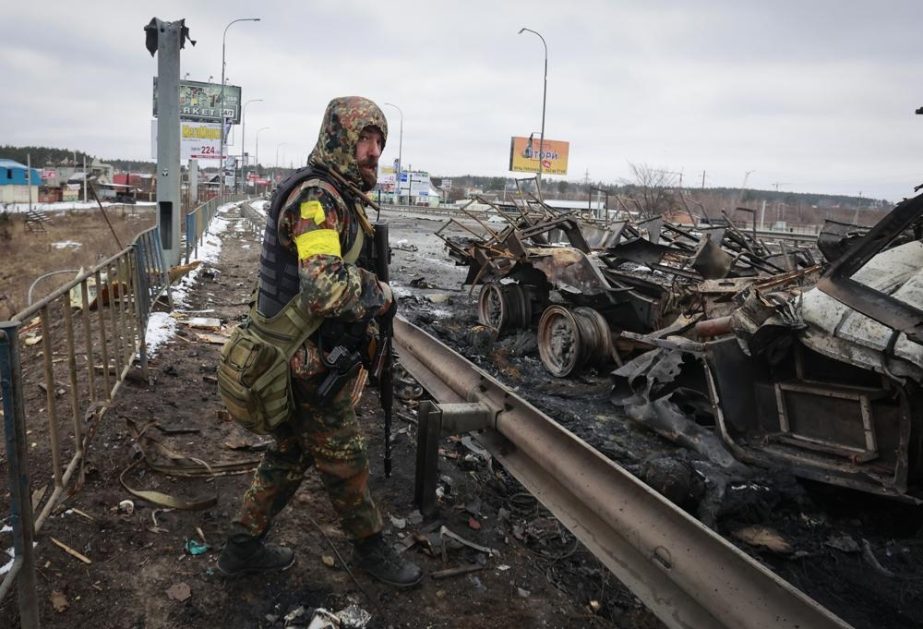 An armed man stands by the remains of a Russian military vehicle in Bucha, close to the capital Kyiv, Ukraine, Tuesday, March 1, 2022.