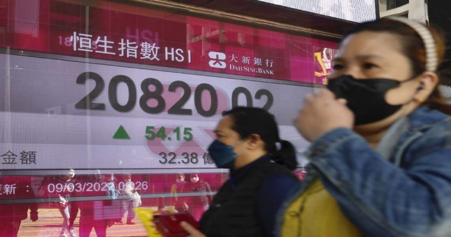 People walk past a bank's electronic board showing the Hong Kong share index at Hong Kong Stock Exchange Wednesday, March 9, 2022.