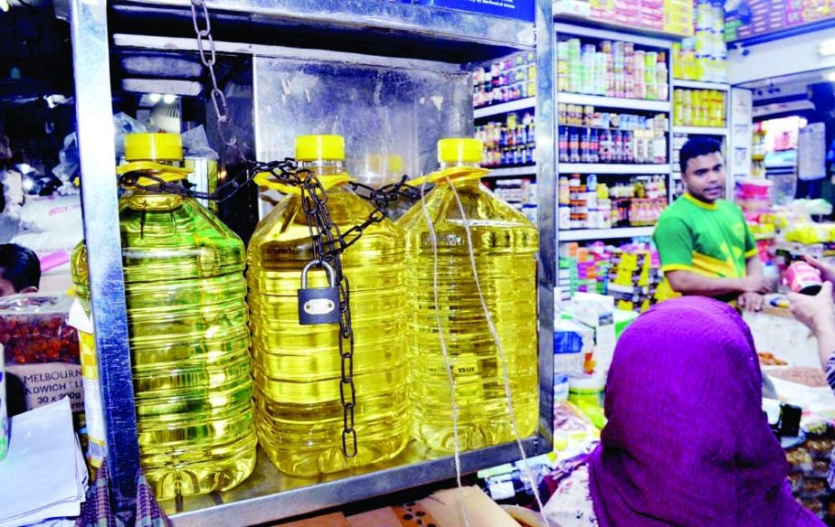 A grocer in the capital’s Karwan Bazar kitchen market on Saturday attends a customer keeping his bottles of edible oil in chains in a bid to foil the attempt of shoplifters as the essential kitchen item turns dearer day by day. NN photo