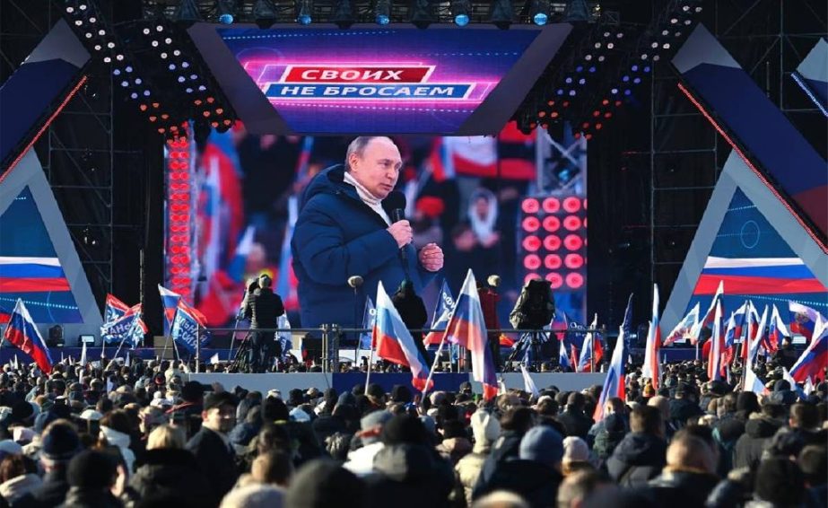 Vladimir Putin seen on the big screen as he delivers his speech at a concert in Moscow, Russia, Friday, March 18, 2022, with a banner reading "For Russia" projected in the backgroud.