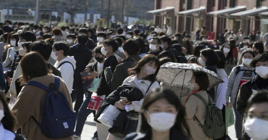 People wearing protective masks to help curb the spread of the coronavirus walk along a square in front of a red brick warehouse Monday, March 21, 2022, in Yokohama, near Tokyo.
