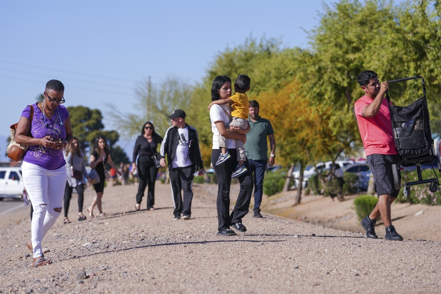 People walk away from a holding area following a shooting at Tanger Outlets mall, Wednesday, March 23, 2022, in Glendale, Ariz.