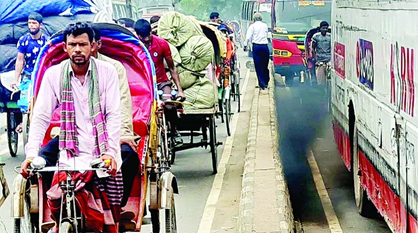 A bus is seen emitting black smoke from its exhaust pipe, rickshaw pullers with passengers moving past on the other side of the road divider. This photo was taken in front of city's Muktangon area on Saturday.