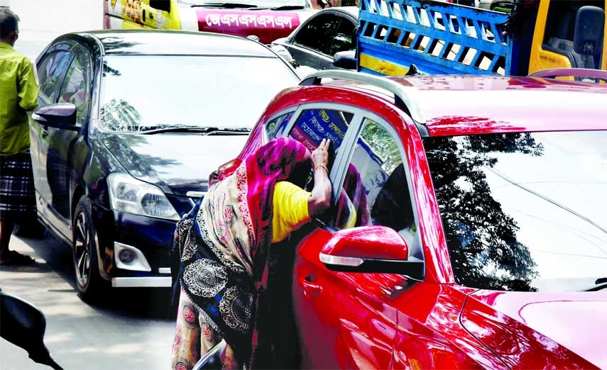A female beggar peeks through the window of a private car to attract someone in front of the Secretariat on Saturday. NN photo