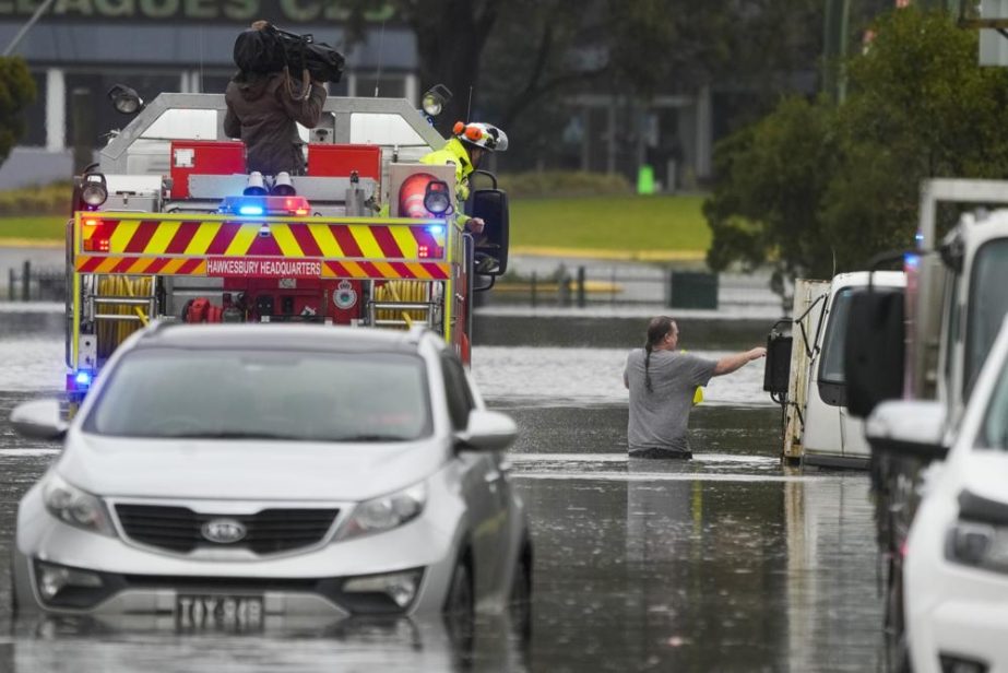A man walks through flood waters back to his home from a fire truck at Windsor on the outskirts of Sydney, Australia, Tuesday, July 5, 2022.
