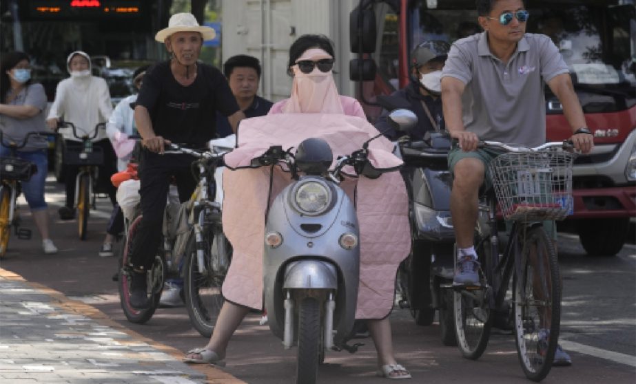 A woman covered up from the sun waits at a traffic junction, Wednesday, July 13, 2022, in Beijing.
