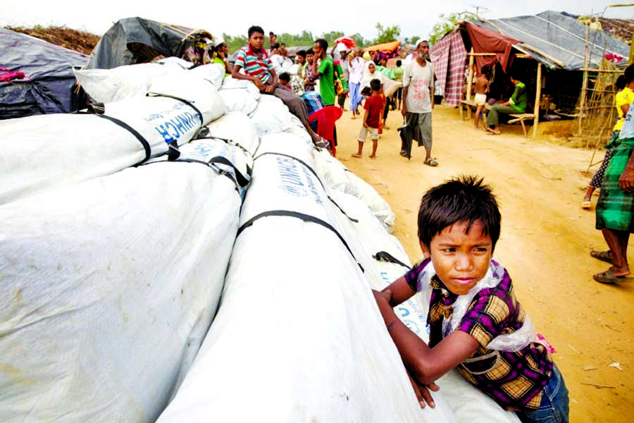 A Rohingya boy leans against UNHCR tarpaulin on Tuesday, waiting to be distributed at Kutupalong refugee camp.